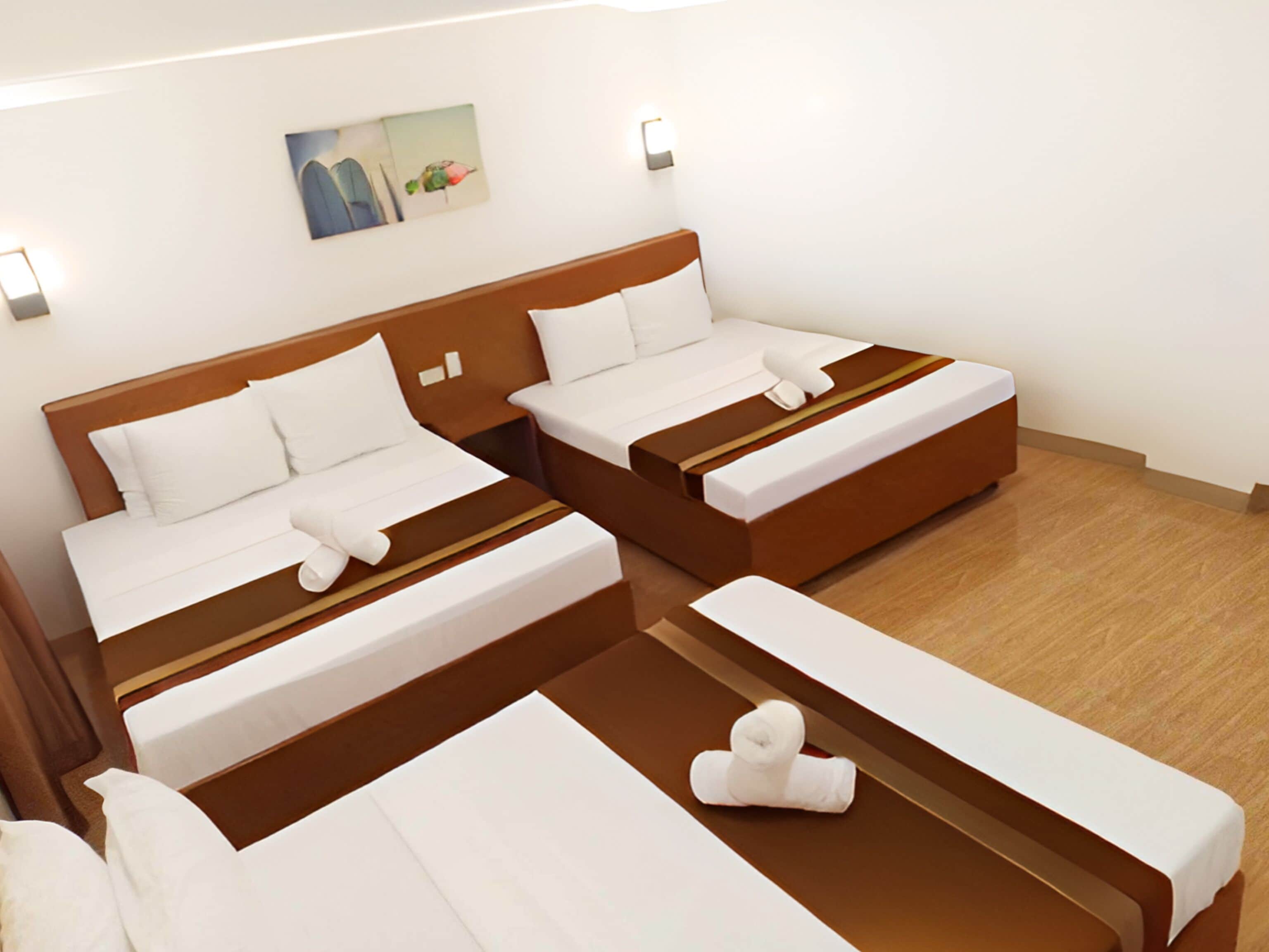 Habitación de hotel con dos camas, un banco y una pequeña mesa.