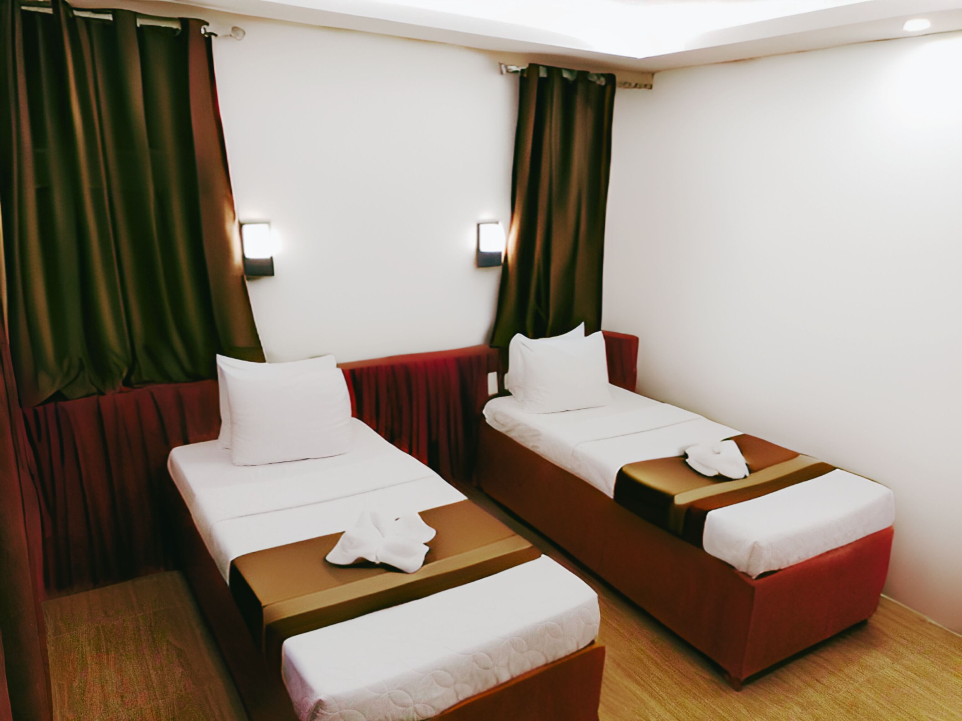 Habitación de hotel con dos camas individuales, cada una con cabecero rojo, ropa de cama blanca y una toalla blanca al pie de la cama.