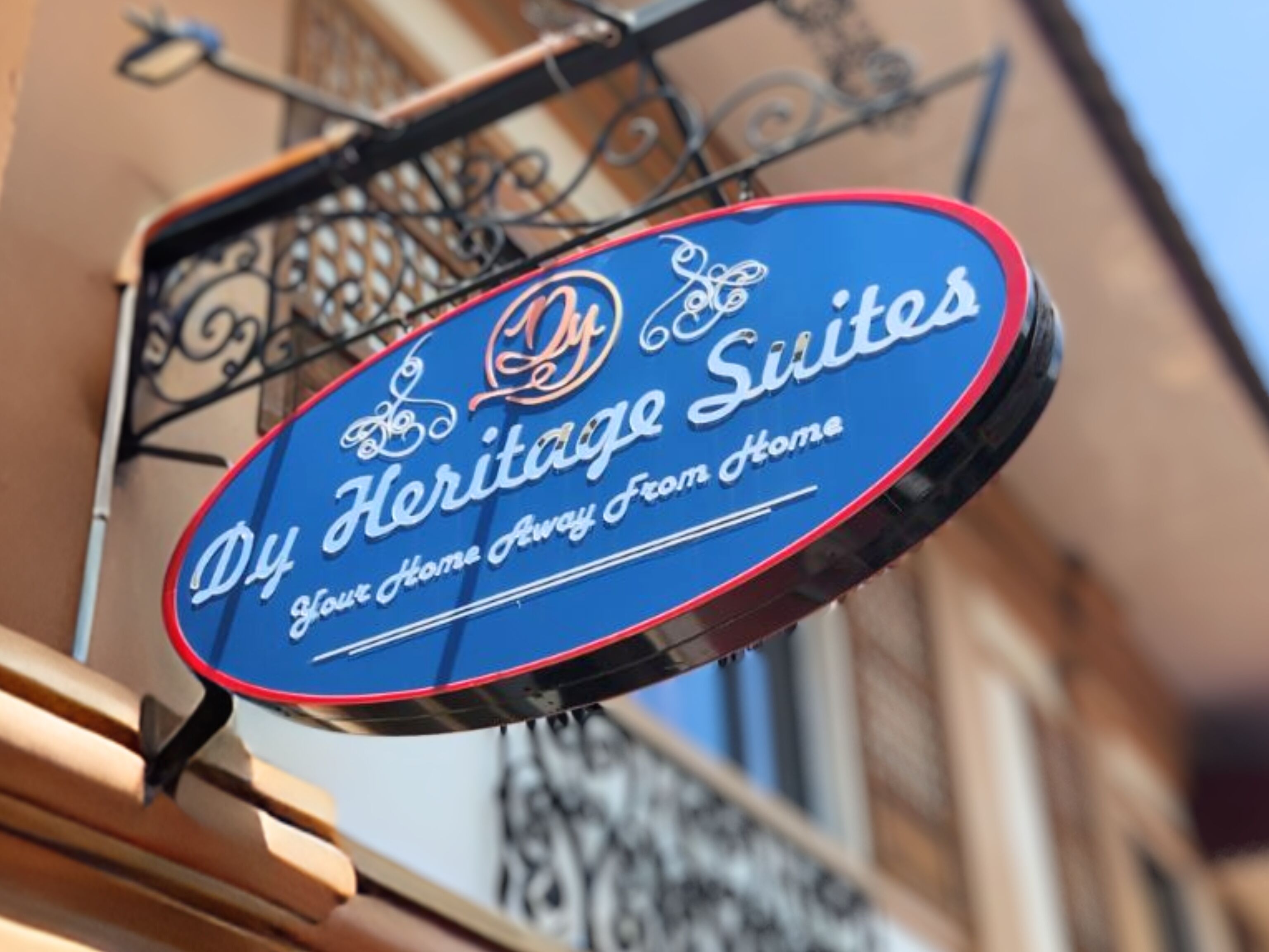 A sign for 'Dy Heritage Suites' with a decorative emblem and the text 'Your Home Away From Home'.
