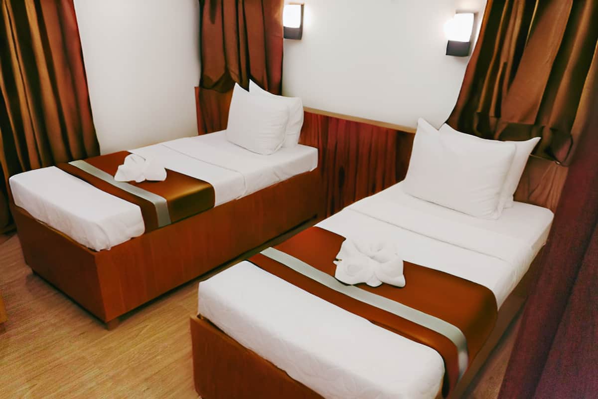 Dos camas individuales con cabeceros de madera y ropa de cama blanca, suelo de madera y cortinas marrones.