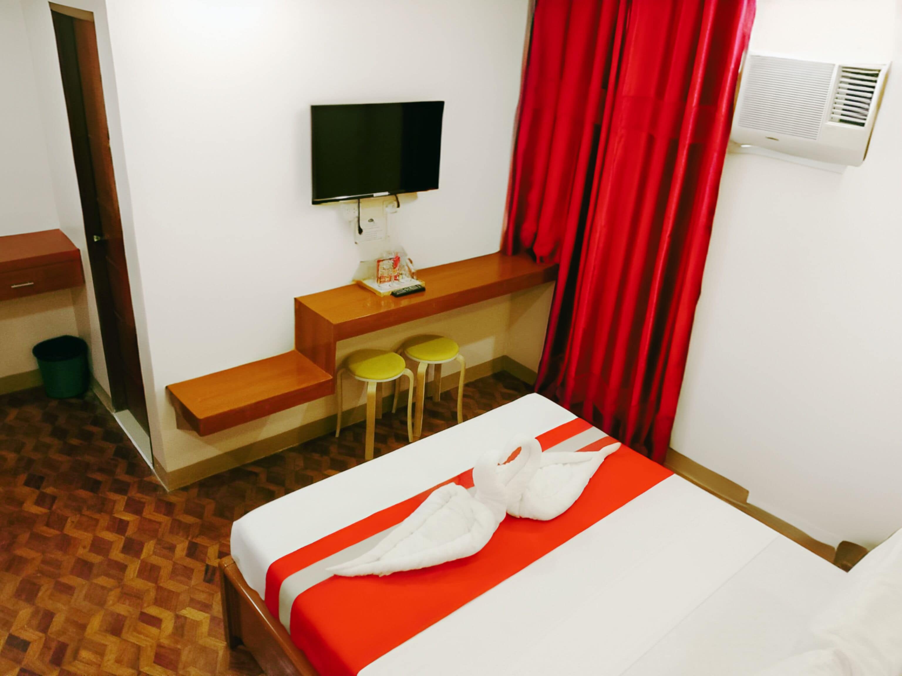 Habitación de hotel con una cama, un escritorio con dos sillas, un televisor y una cortina roja.