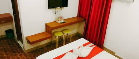 Habitación de hotel con una cama, un escritorio con dos sillas, un televisor y una cortina roja.