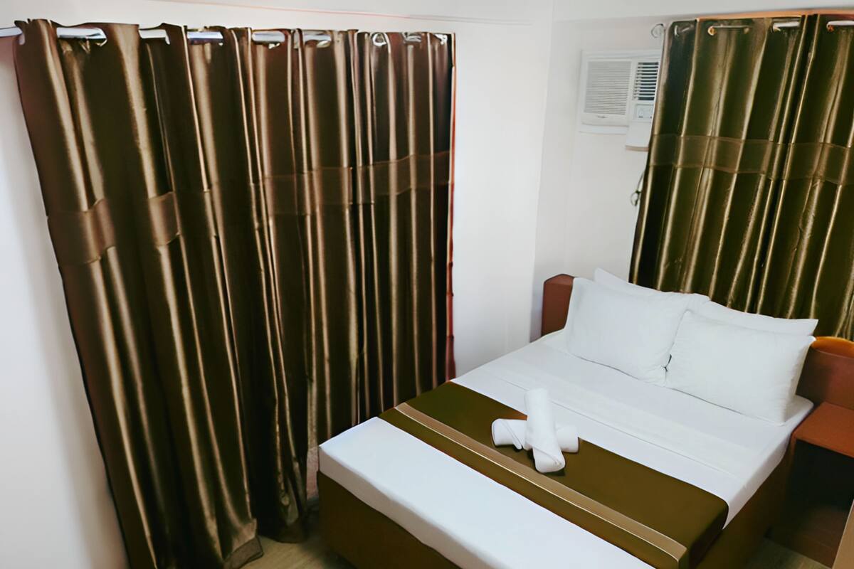 Una habitación de hotel con cama, cortinas y una ventana con aire acondicionado.