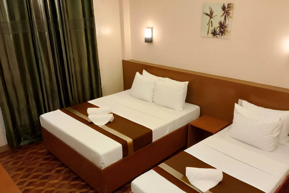 Habitación de hotel con dos camas, piso de madera, una lámpara de pared y un cuadro.
