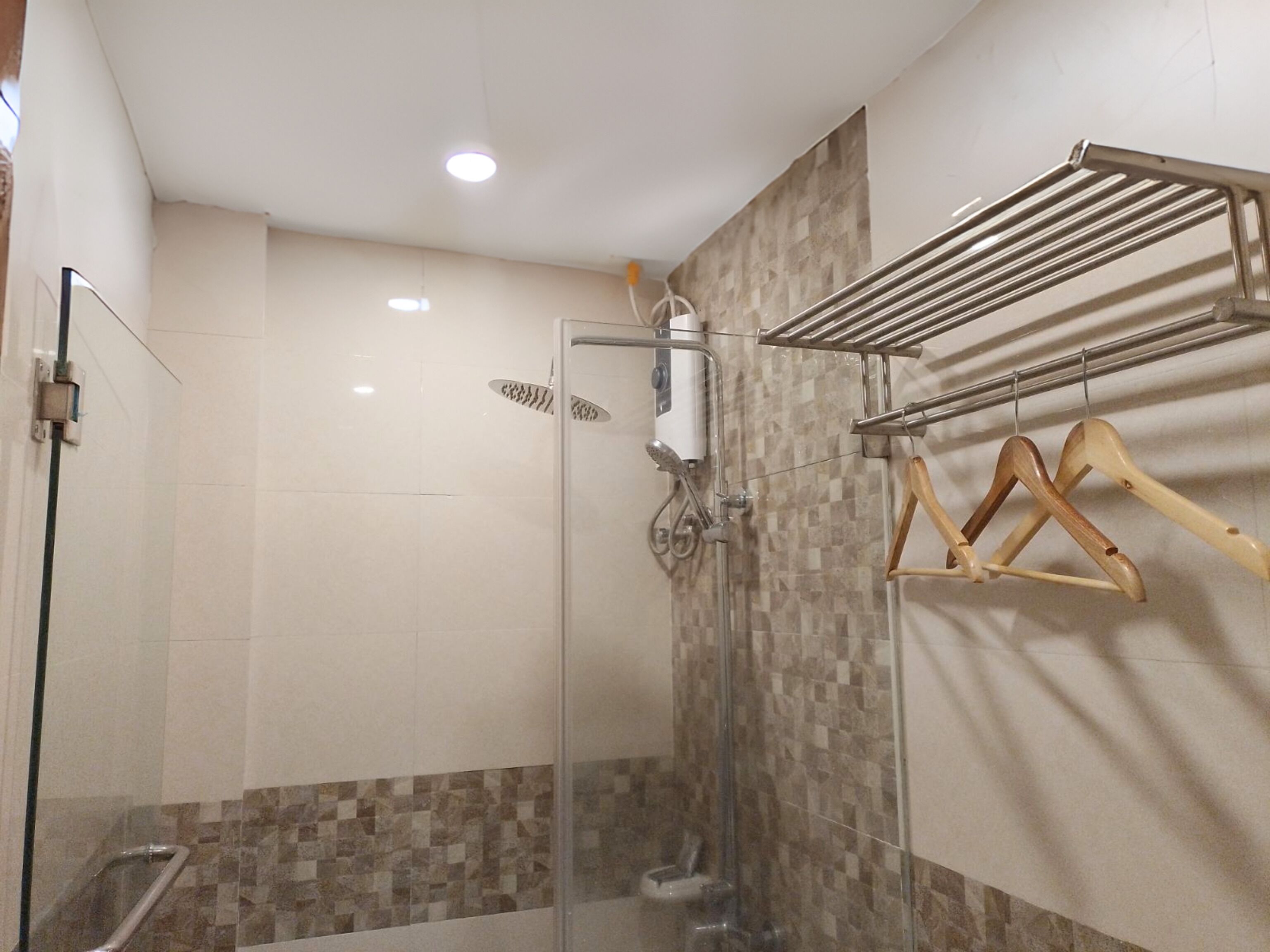 A shower area with a glass door, a towel rack with wooden hangers, and a tiled wall with a checkered pattern.