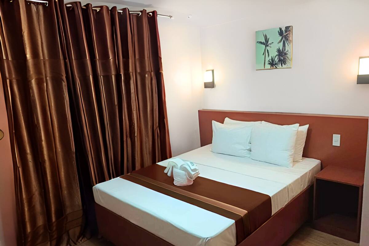 Habitación de hotel con cama, mesita de noche, cortina e iluminación empotrada en la pared.