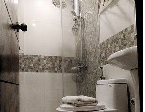 A bathroom with a glass-enclosed shower, a toilet, and a sink. - Dy Heritage Suites (Vigan)