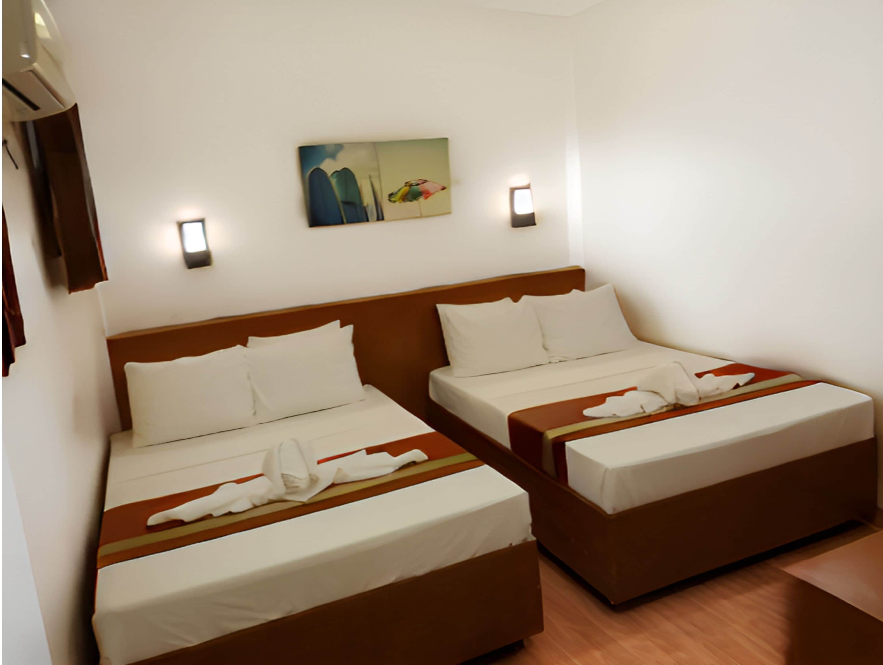 A hotel room with two single beds, a wooden headboard, white bedding, a painting on the wall, and two wall-mounted lights.