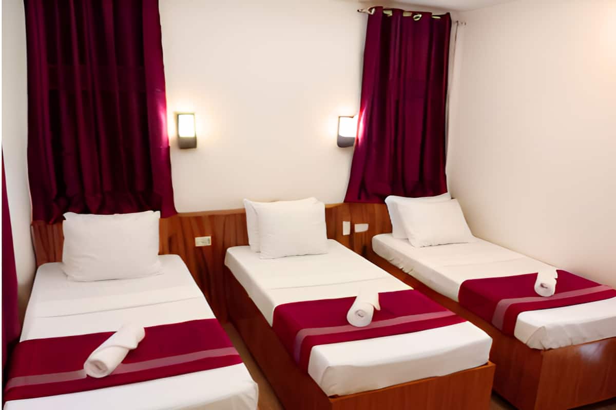 Habitación de hotel con tres camas individuales, cada una con ropa blanca y detalles en rojo.