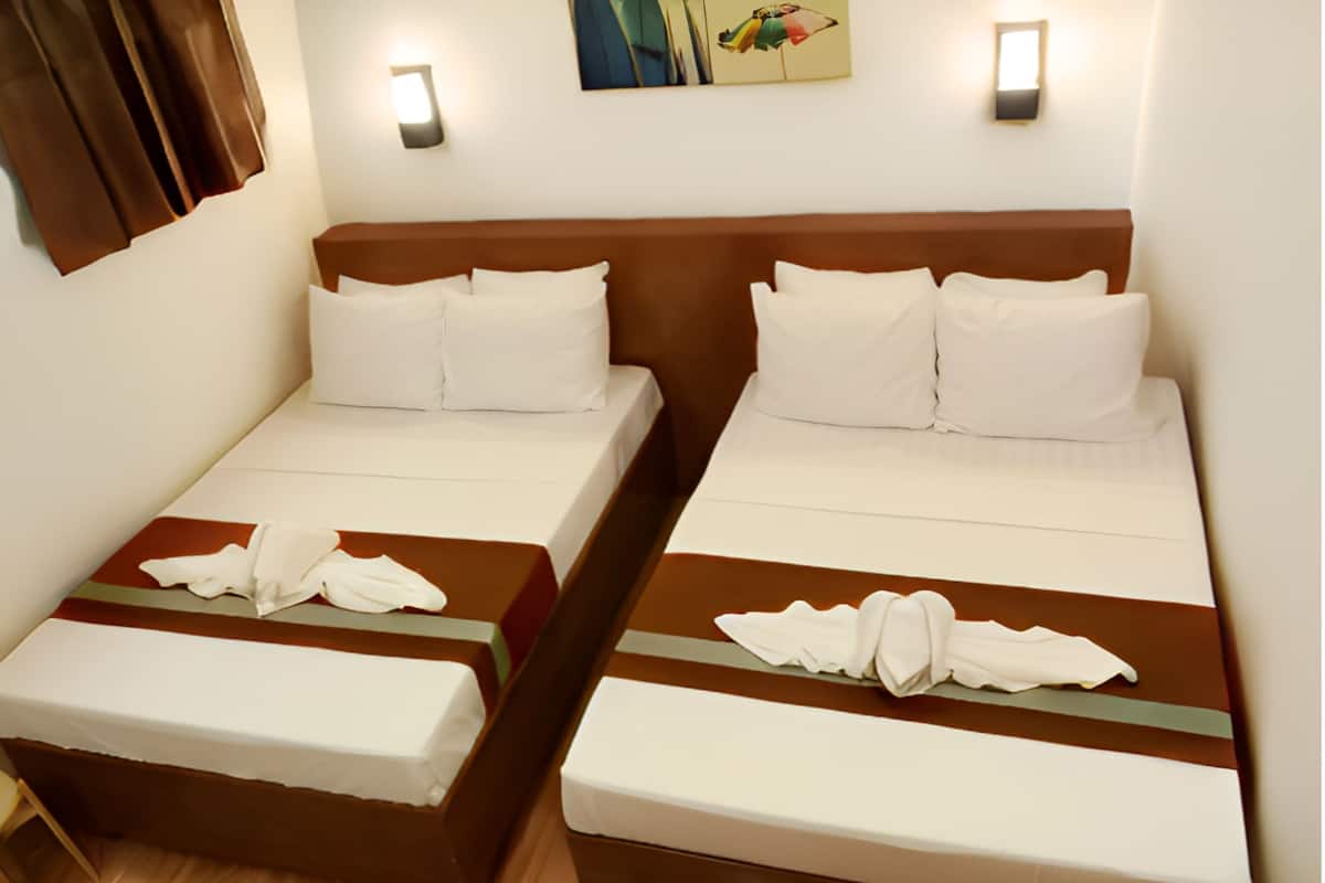 Habitación de hotel con dos camas individuales, cada una con cabecero marrón, ropa de cama blanca y una mesita con una toalla.