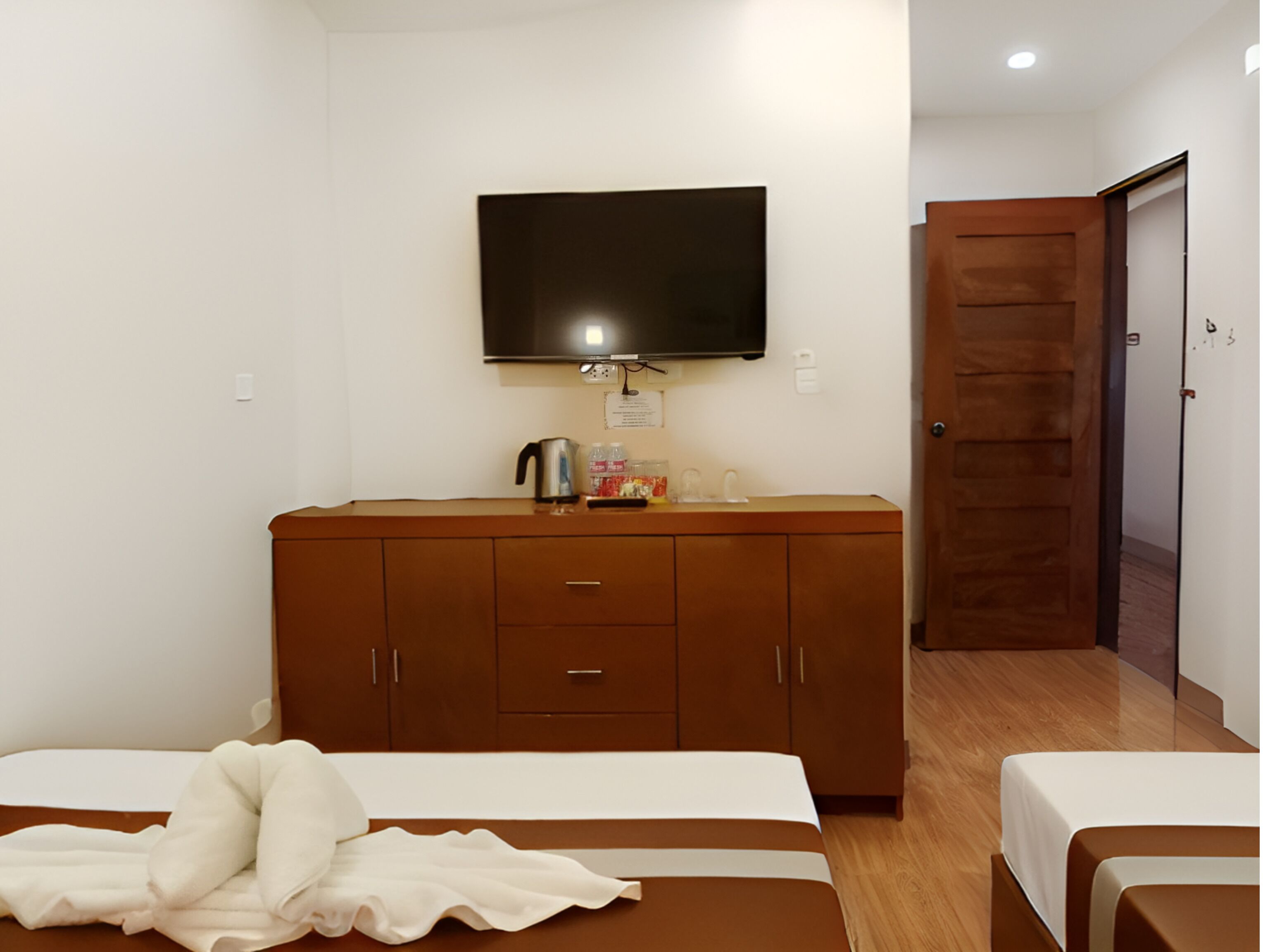 A hotel room with a bed, a TV mounted on the wall, a wooden dresser, and a door.