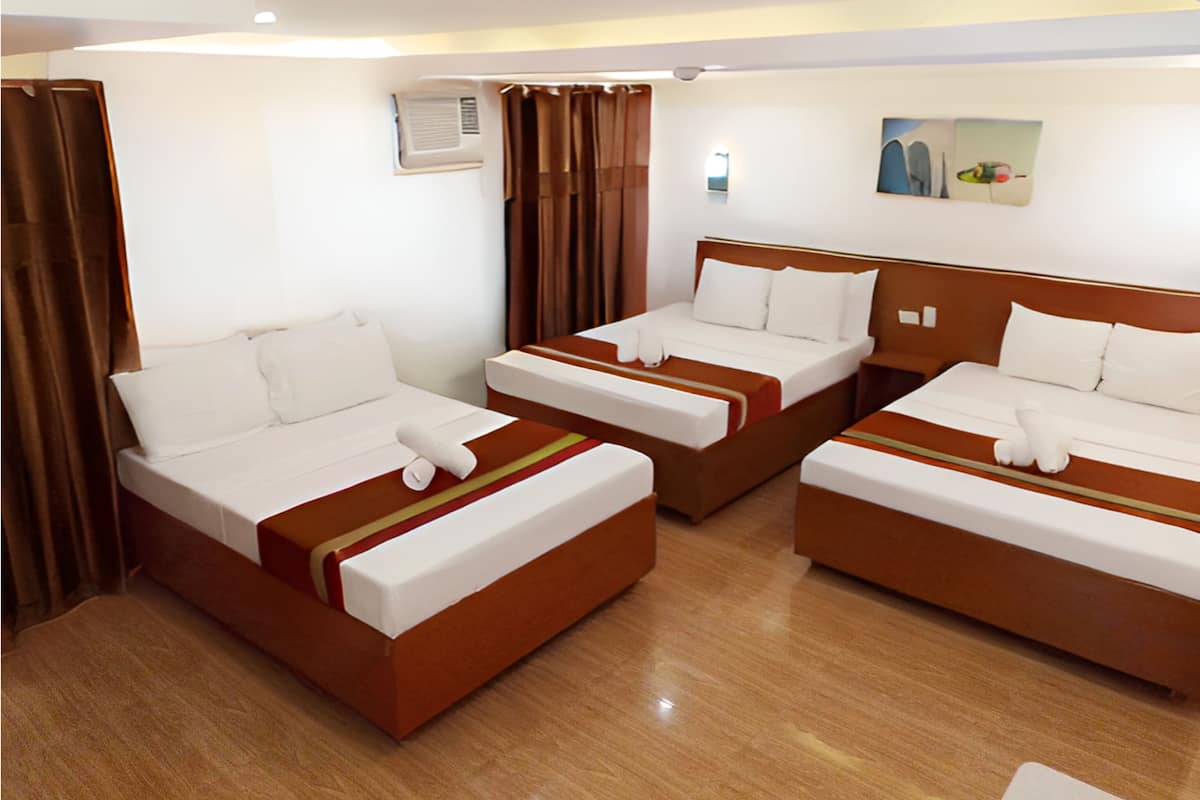 Habitación de hotel con tres camas dispuestas en fila, cada una con ropa blanca y cabeceros marrones.