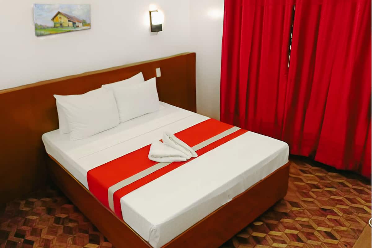 Una cama bien tendida con ropa blanca y un detalle rojo, un cabecero de madera, un cuadro en la pared y cortinas rojas.