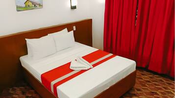 Una cama bien tendida con ropa blanca y un detalle rojo, un cabecero de madera, un cuadro en la pared y cortinas rojas.