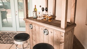 Una barra de madera con dos taburetes, una botella de licor y vasos sobre la encimera.