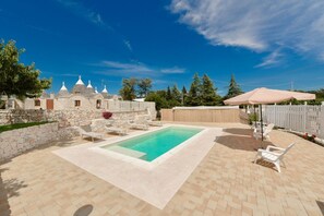 A backyard with a swimming pool, stone walls, and outdoor furniture.