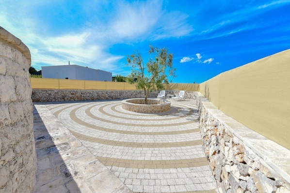 A courtyard with a circular stone pattern, a tree, and a white building in the background.