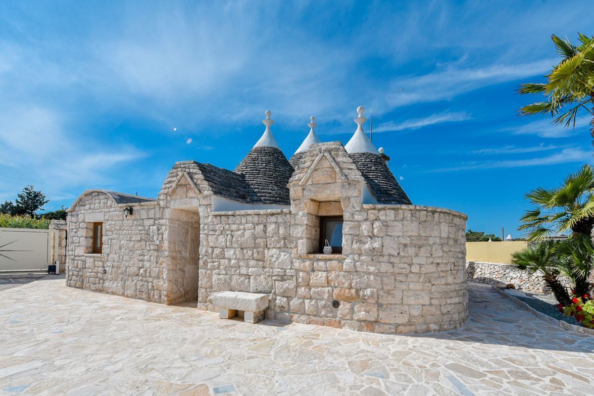A stone building with multiple conical roofs, a bench, and a paved area.