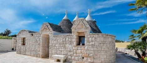 A stone building with multiple conical roofs, a bench, and a paved area.