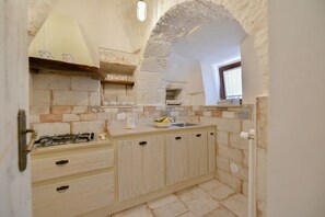 A rustic kitchen with stone walls, a gas stove, wooden cabinets, and a window.
