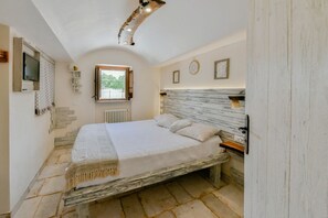 A bedroom with a bed, a window, a television, and a radiator.