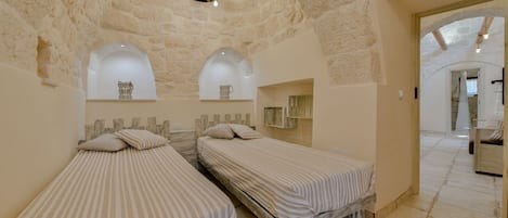 A room with two beds, a stone ceiling, and a chandelier.