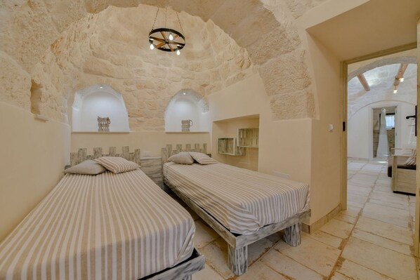 A room with two beds, a stone ceiling, and a chandelier.