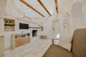 A rustic room with exposed stone walls, a wooden bench, a sofa, a television, and a fireplace.