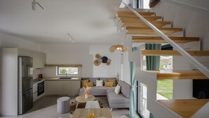 A modern kitchen with a built-in oven and refrigerator, a dining area with a wooden table and chairs, and a staircase with wooden steps.