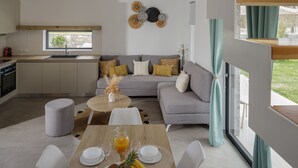 A modern kitchen with a built-in oven, a dining area with a table set for breakfast, and a grey sofa with cushions.