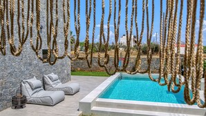 A pool area with a stone wall, grey lounge chairs, and a hanging rope feature.