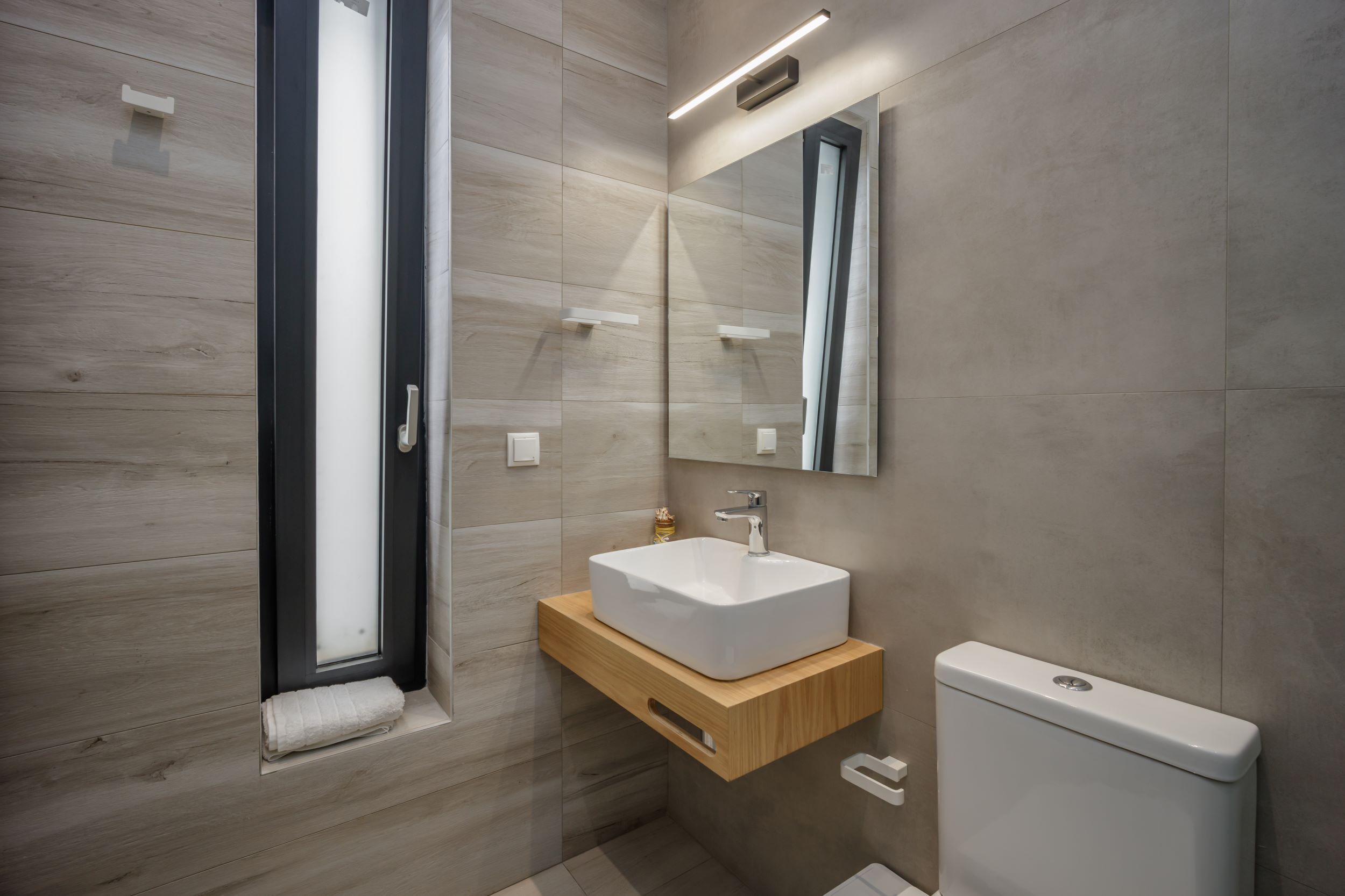 A modern bathroom with a wooden vanity, a white sink, and a toilet.