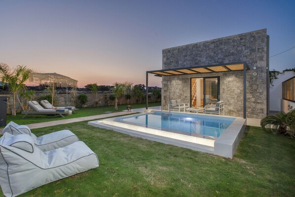 Ein modernes Haus mit Swimmingpool, Sitzgelegenheit im Freien und Blick auf eine entfernte Bebauung.