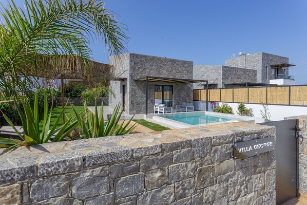 En moderne villa med en stenvæg, swimmingpool og et overdækket udendørs siddeområde.