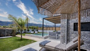 A modern outdoor patio with a pool, lounge chairs, and a stone wall backdrop.