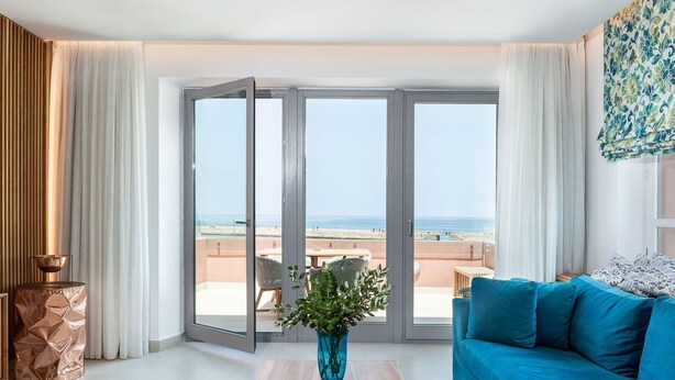 A modern living room with a large sliding glass door leading to a balcony with a beach view.