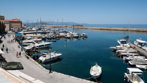A marina with boats docked along the waterfront, a pedestrian walkway, and a building with a red roof.