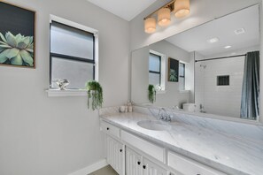 A modern bathroom with a large mirror, white marble countertop, and a window with a plant. - Great Home with Southern Charm and Great Space (Frisco)