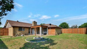 Une maison à deux étages, avec une façade en briques, une cheminée et une cour arrière clôturée.