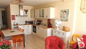 A compact kitchen with white cabinets, a dining table, and a red chair. - Le Bel Horizon - Face Mer (Les Sables-d´Olonne)