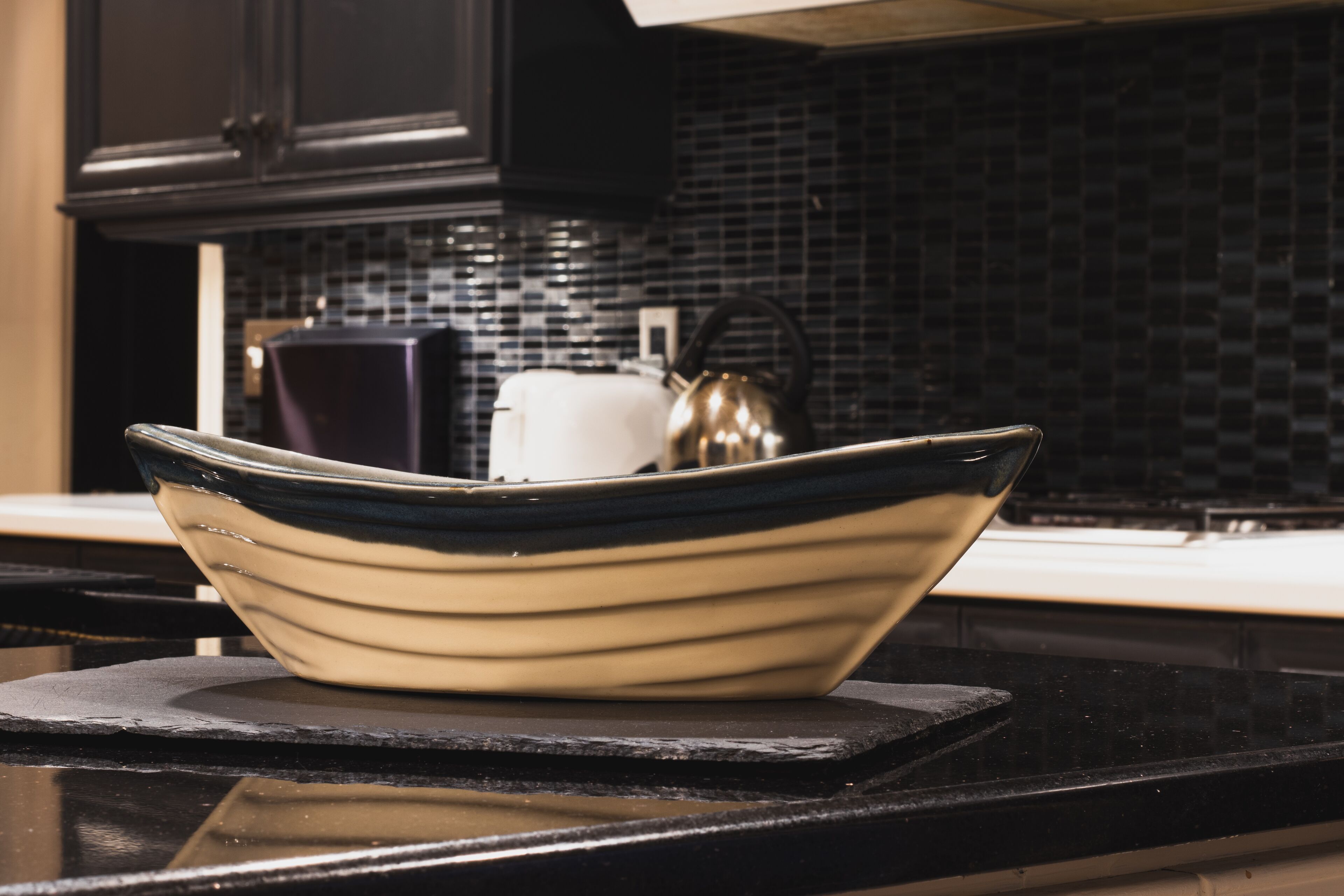 A kitchen with a black countertop, a white kettle, and a black and white bowl.