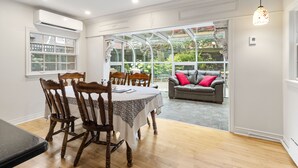Un comedor con mesa y sillas, un patio con cerramiento de vidrio y sofá, y una lámpara colgante.