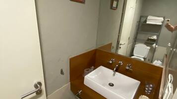 A bathroom with a wooden vanity, a white sink, a mirror, and a towel rack.