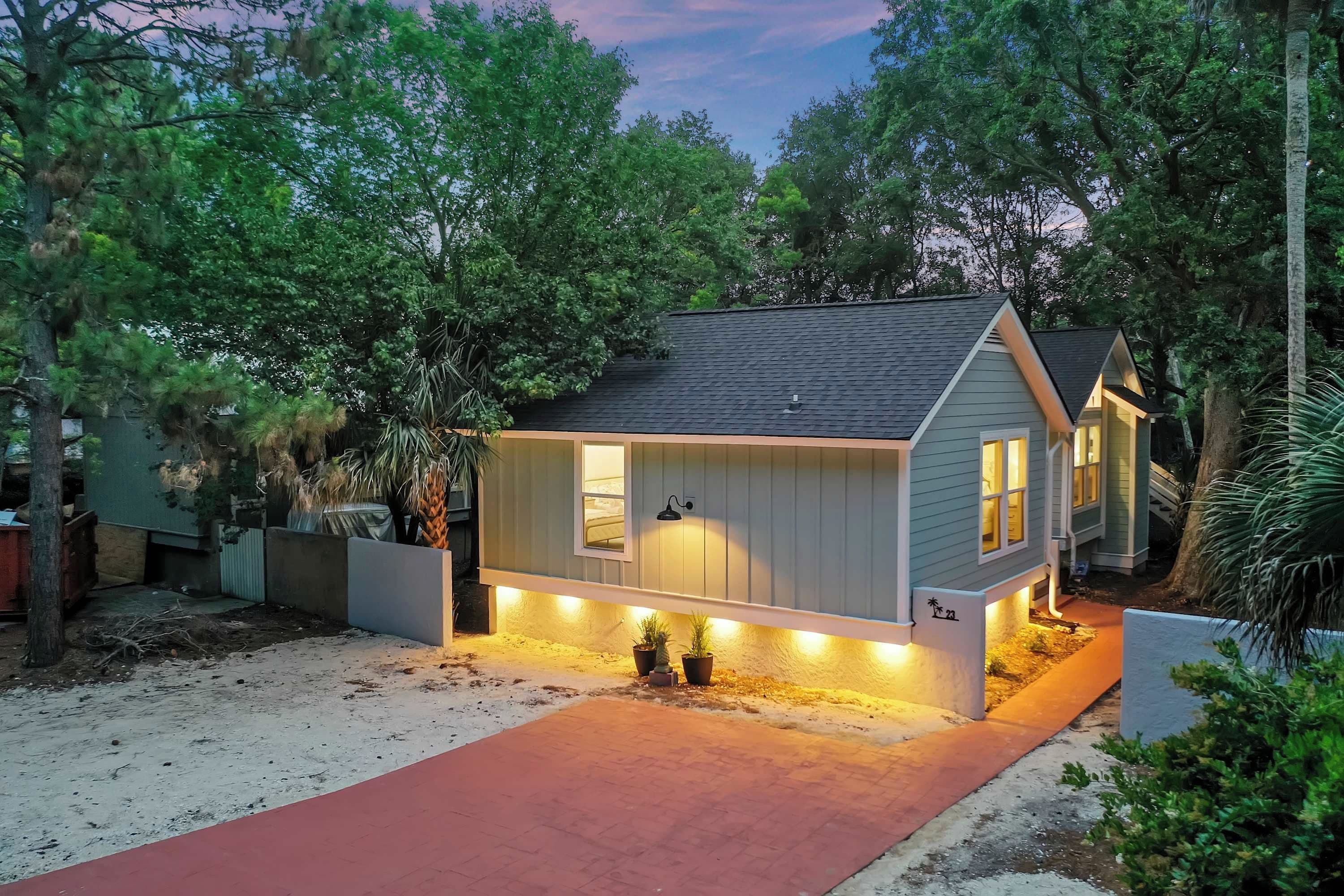 A single-story house with a dark roof, a front porch, and a red pathway leading to the entrance.
