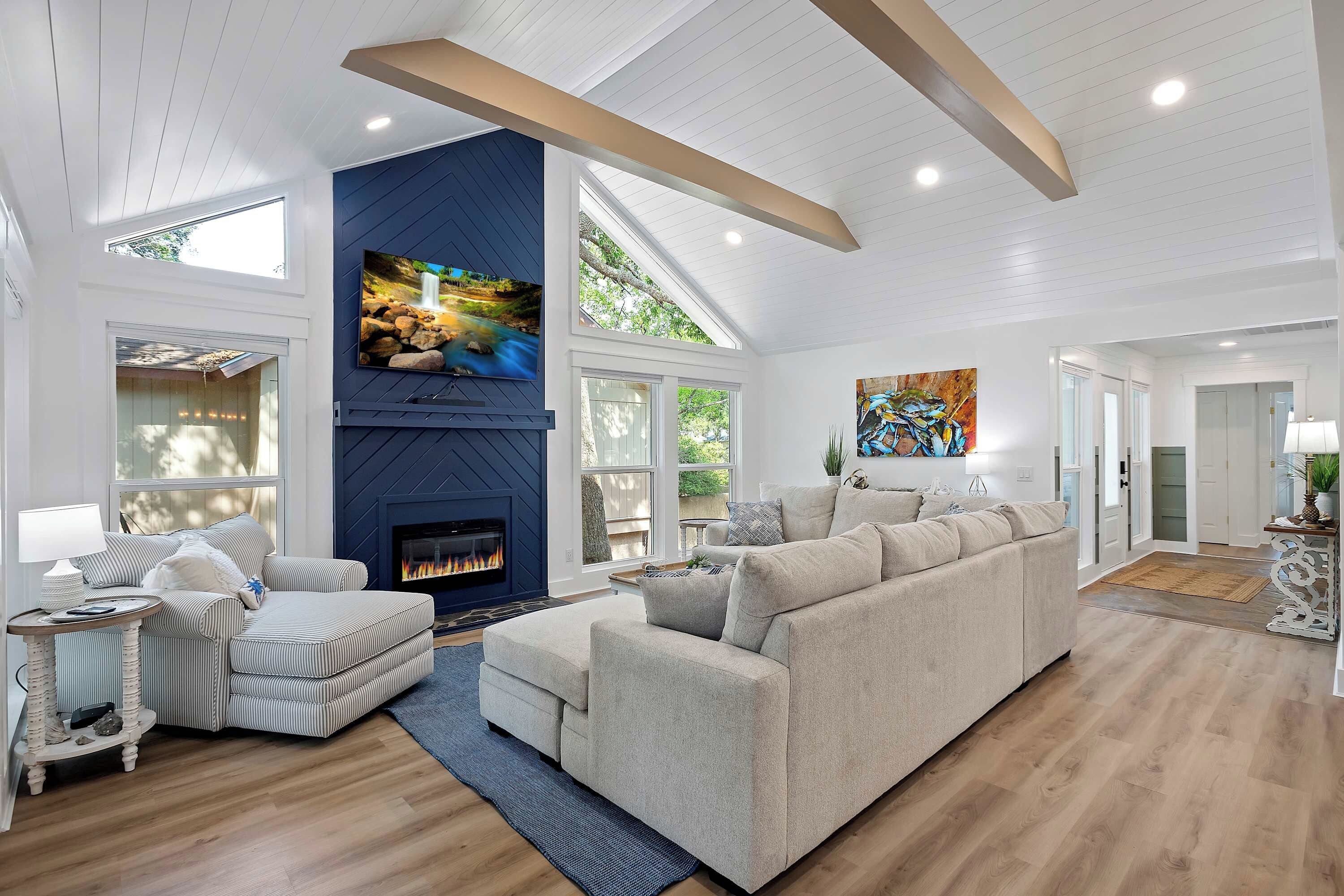 A spacious living room with a fireplace, a large sofa, and a television mounted on the wall.