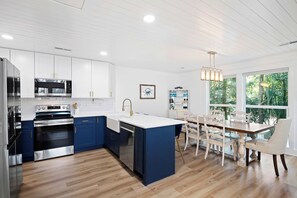 A modern kitchen with white cabinets, stainless steel appliances, and a blue island. - Stunning Renovated Designer Home At The Beach! (Isle of Palms)
