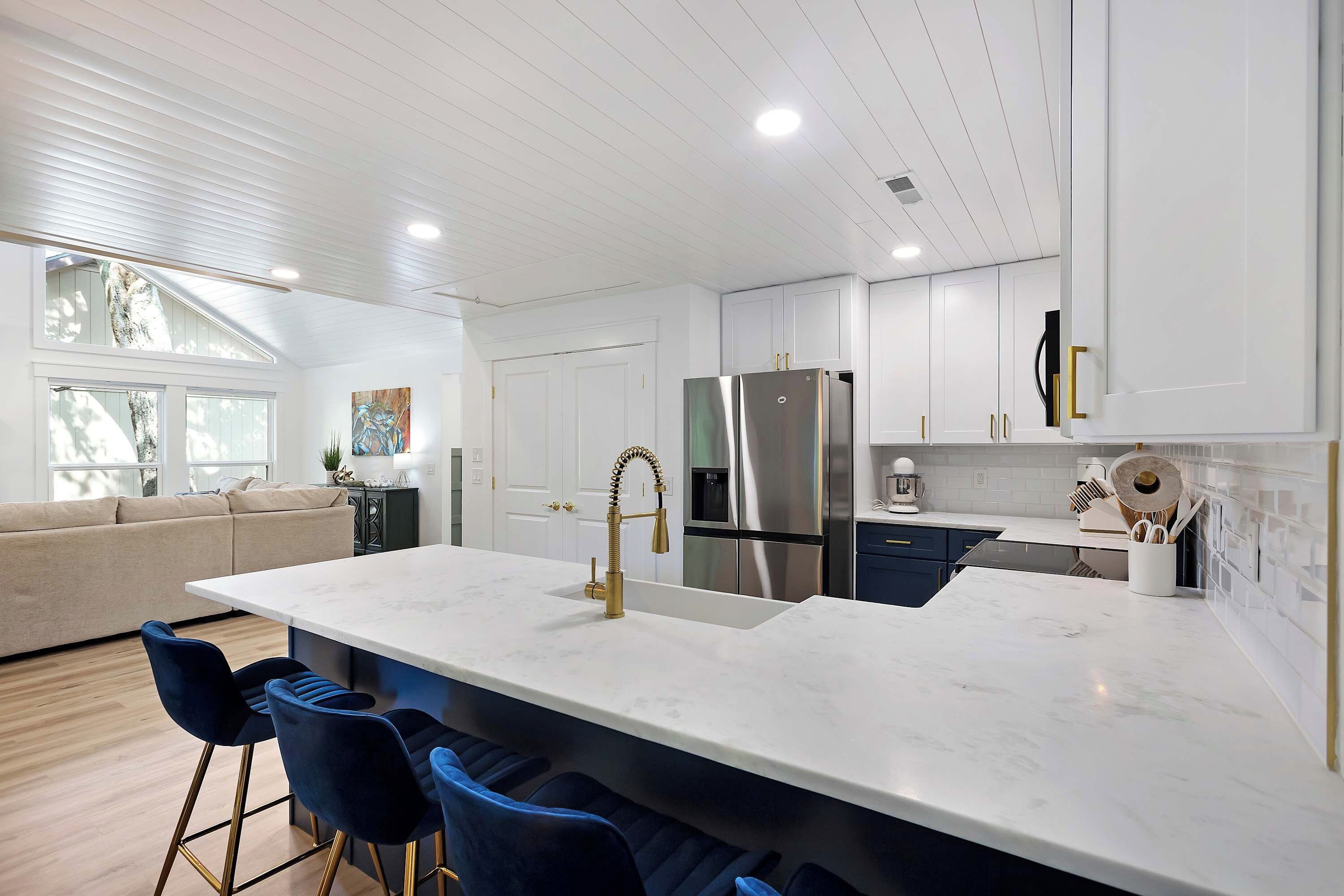 A modern kitchen with white cabinetry, a large island with bar stools, and a built-in stainless steel refrigerator.