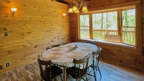 A wooden cabin interior with a round dining table, wooden walls, and a large window with a view of trees. - Private Cabin with Pond on Family Farm (Belleville)