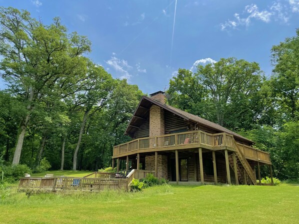 A rustic log cabin with a balcony, surrounded by lush greenery and trees. - Private Cabin with Pond on Family Farm (Belleville)