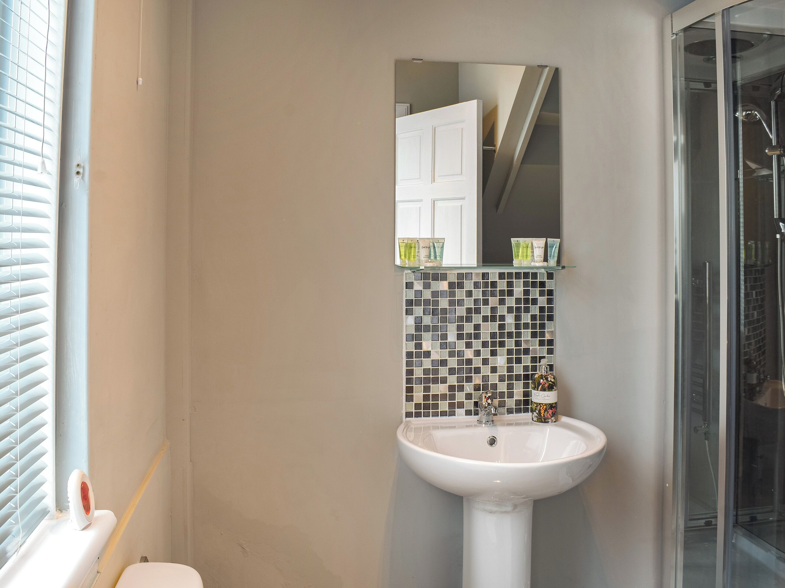 Ein Badezimmer mit einem weißen Waschbecken, einer gefliesten Rückwand und einer Duschkabine aus Glas.
